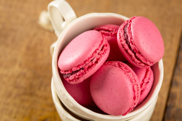 A close-up of colorful  pink strawberry macaroons, piled high in coffee cups.