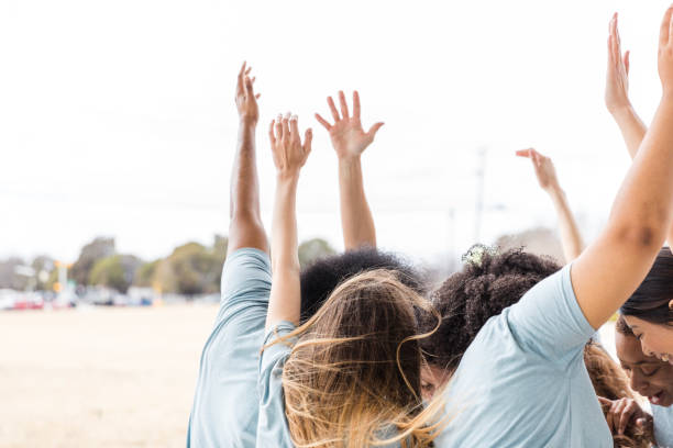 Multiracial group of adults expressing joy and unity.  Arms raised high.