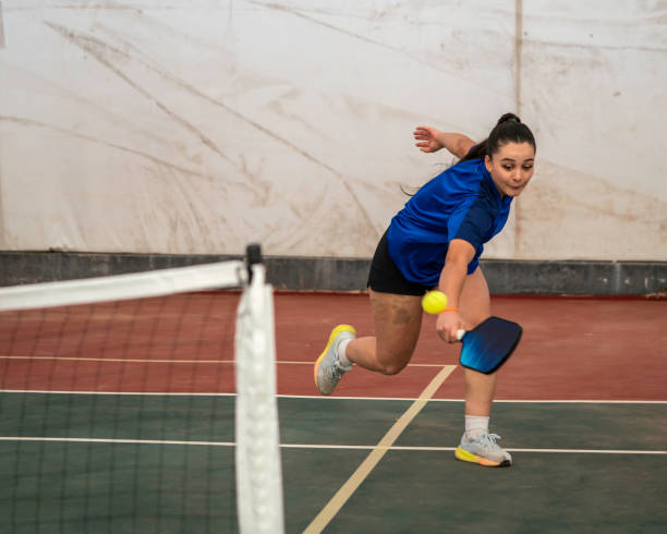 female pickleball player is shooting backhand on hardcourt next to sport net ball is on air horizontal pickleball still stock photo