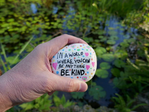 istock Be kind message painted on kindness rock held in hand in front of tropical pond 2200869605