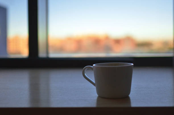 istock White coffee cup sitting on a window sill during sunrise 2200880852