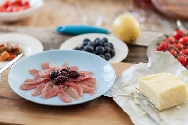 Butter board preparing, softened butter in wrapping with parma ham slices on wooden serving board