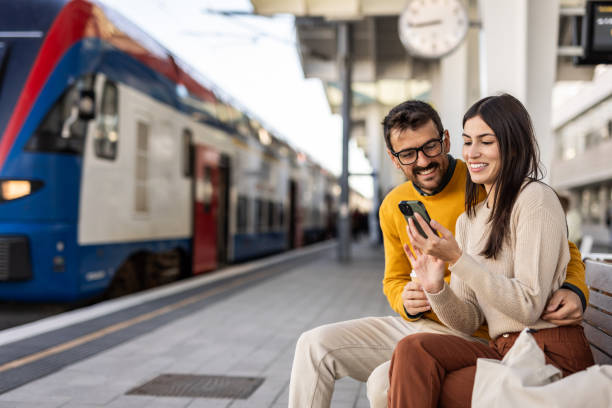 istock Smiling tourist couple using smartphone and drinking coffee at train station 2200887173