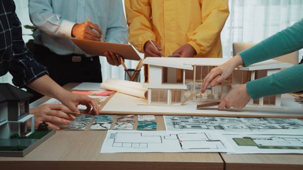 istock Collaborative Architectural Design Meeting with Model, Blueprints, and Plans on Table with Hands of Professionals Engaged in Discussion and Planning SACTR 2200887936