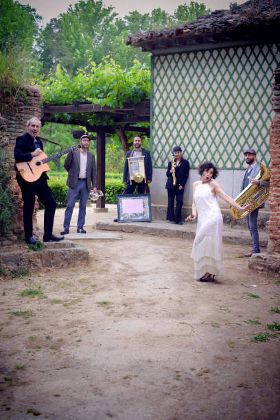 Jazz group of six people with different musical instruments, dressed in retro style, posing and dancing in the garden of a house.