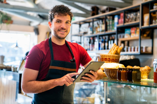 istock Waiter at a coffee shop holding a digital tablet and smiling 2200892625