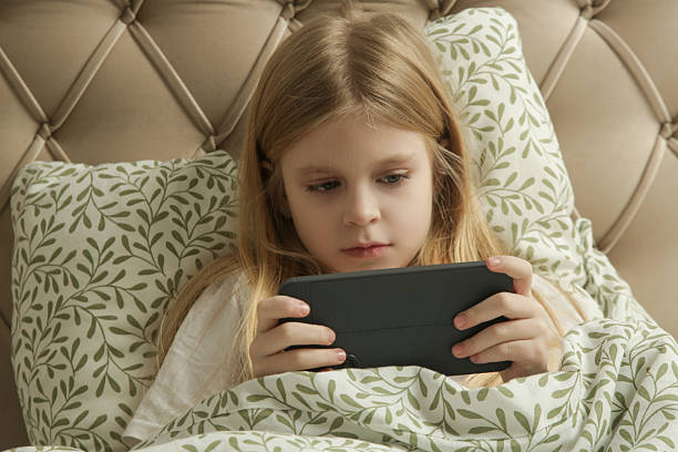 istock Cute little girl using smartphone at home, looking at screen before sleep time 2200901543