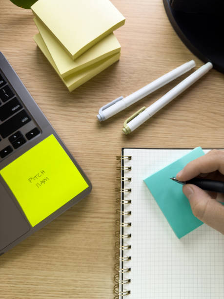 istock Home Office Desk With Stack Of Yellow Post-its®, Pens, Laptop With Post-it® Reminder, And Hand Writing On Notebook 2200907792