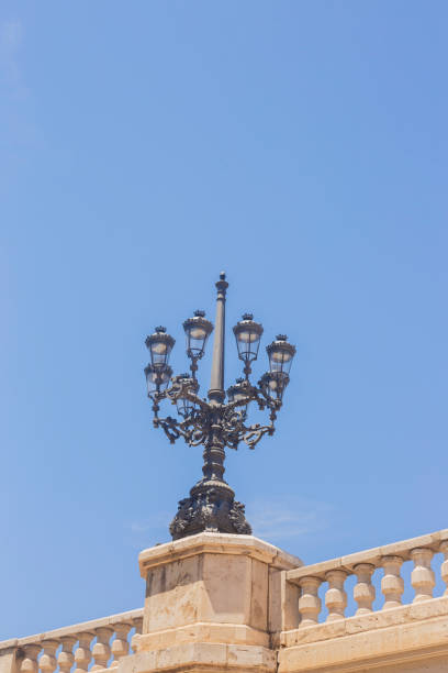 black iron lampost with lights in Valencia, Spain. There is a blue sky in the background.