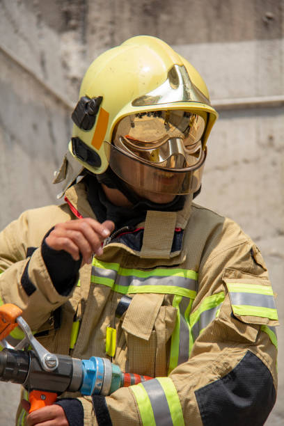 A Caucasian firefighter in his late 20s standing in front of a fire truck, wearing a fire protection suit and helmet.