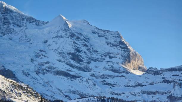 istock A majestic snow-covered mountain peak rises against a clear blue sky. Sunlight highlights the rugged cliffs and icy slopes, creating a breathtaking alpine landscape with a crisp winter atmosphere. 2200914657