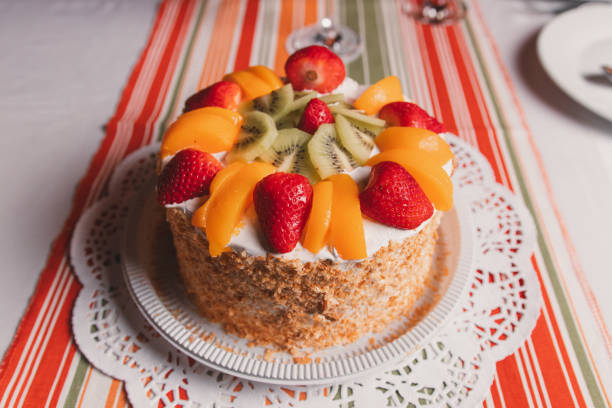 Cake with whipped cream and fruit served on a plate at a long table.