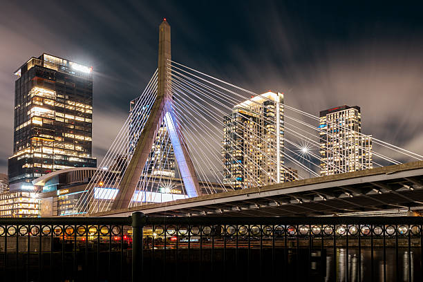 Boston, Massachusetts – October 19, 2023: Long-exposure night view of the Leonard P. Zakim Bunker Hill Memorial Bridge and TD Garden arena, with surrounding modern buildings brightly illuminated across the Charles River.