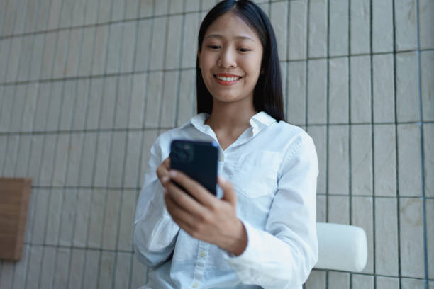 istock Young woman smiling while using smartphone in modern indoor setting with natural light and neutral background 2200921407