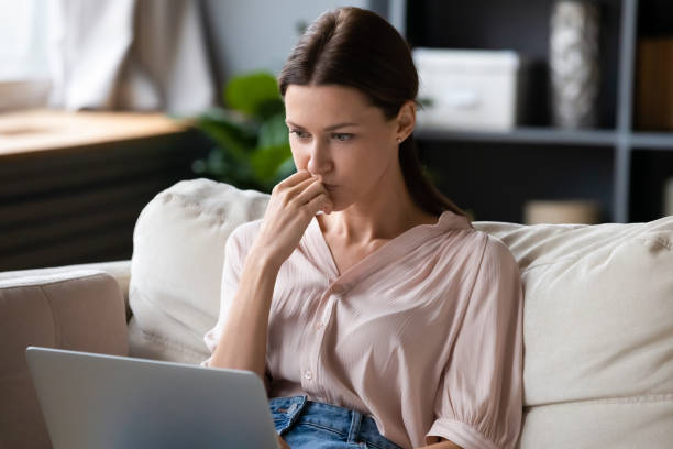 Female sitting on couch looking at computer screen feels confused