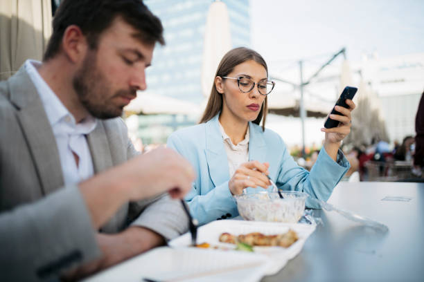 istock Businesswoman using mobile phone while having lunch with colleague 2200933600