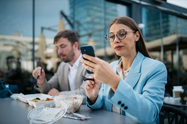 Businesswoman using smartphone while having lunch break outdoors with colleague