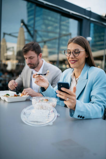 istock Businesswoman using smartphone while eating lunch outdoors with colleague 2200933638