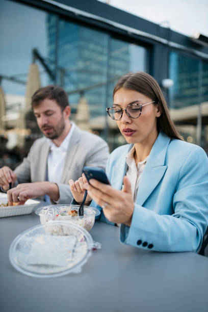 istock Businesswoman using smartphone while having lunch outdoors with her colleague 2200934050