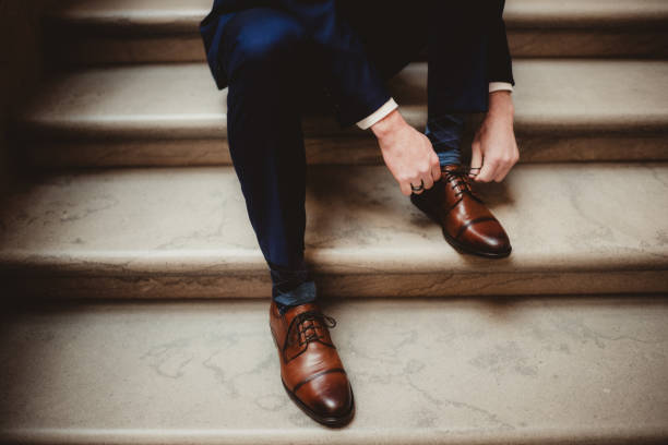 Man in suit tying brown leather dress shoes on elegant marble stairs