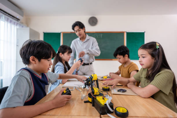 istock Group of students learning in a robotics class at elementary school. Enthusiastic young schoolchildren sitting at table, listening to their teacher explain and teach lesson on robotics in classroom. 2200950359