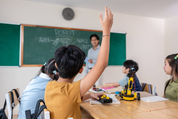 istock Group of students learning in a robotics class at elementary school. Enthusiastic young schoolchildren sitting at table, listening to their teacher explain and teach lesson on robotics in classroom. 2200950368