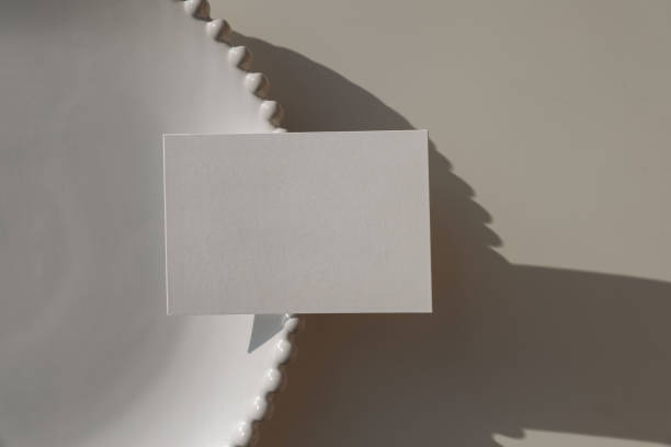 istock Blank horizontal greeting card, invitation mockup. Business card in sunlight on white decorative plate. Beige table background. Long soft shadows overlay. Summer minimal template. Flat lay. Top view. 2200954466