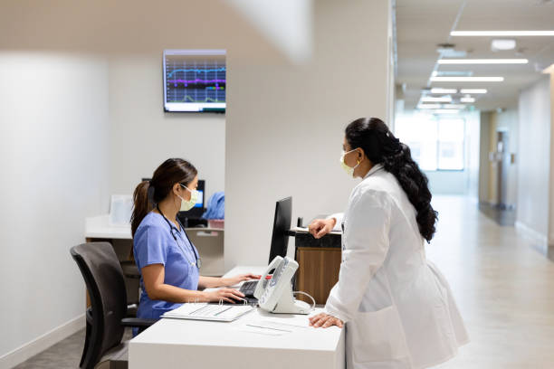 istock Two Female Doctors in Lab Coats Having a Discussion at Hospital Reception 2200955947