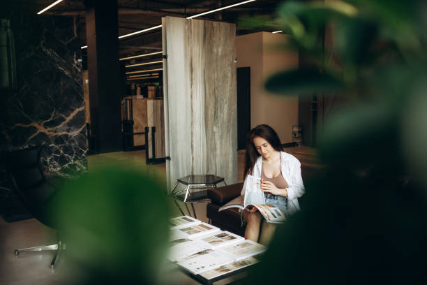 Happy brunette female interior designer choosing flooring tile color texture samples at store shop. Woman architect choice floor and wall finishing material for architecture and construction industry