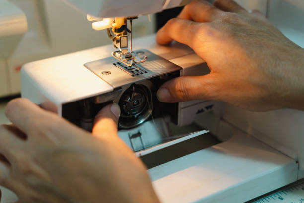 istock Close-up of hands threading a sewing machine bobbin, preparing the machine for sewing. 2200960920