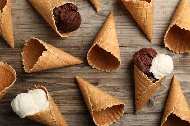 istock Ice cream scoops in wafer cones on wooden table, flat lay 2200966873