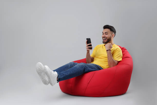 istock Happy young man using smartphone on bean bag chair against grey background, space for text 2200975218