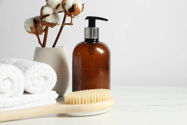 istock Different bath accessories and cotton flowers in vase on light table against white wall, space for text 2200986527