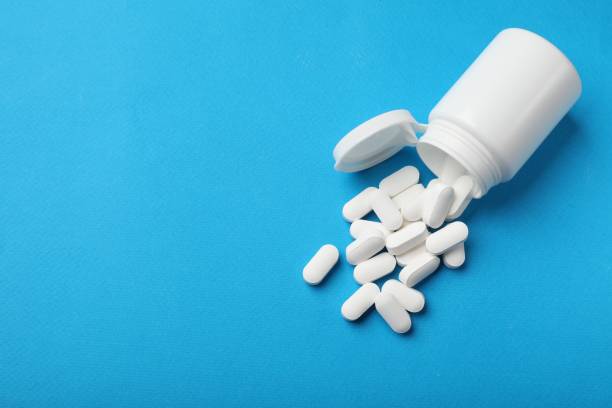 istock Vitamin pills and bottle on light blue background, top view. Space for text 2200986555