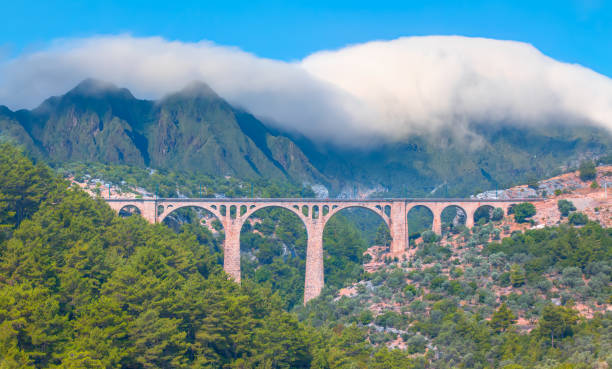 There is a large mountain range in the background with clouds covering the sky - Varda Railway bridge - Adana, Turkey