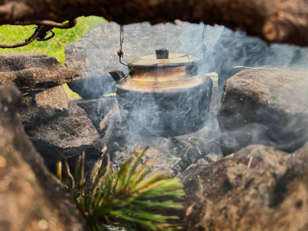 Blackened kettle heating over campfire. Smoke swirls around kettle, and hint of green pine needles.