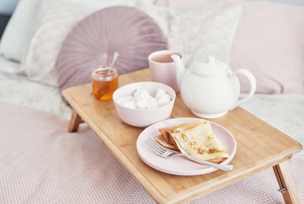 istock Breakfast in bed in hotel room. Accommodation. Breakfast in bed with tea cup with pancakes on tray on bed background top view. Copy Space. Romantic valentine's day breakfast. Cozy breakfast Maslenitsa 2201004136