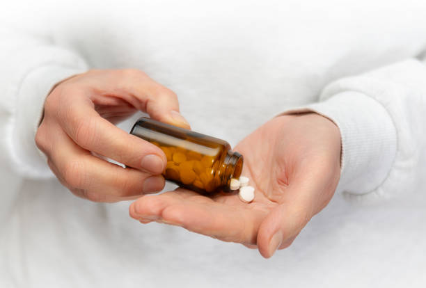 istock Person pouring tablets from a brown bottle into their hand in a well-lit room 2201006334