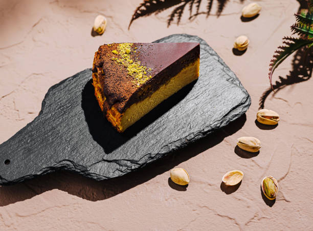 Delightful slice of layered cake served on a rustic black slate board with decorative green leaves in natural light