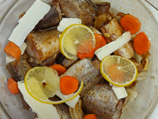 Fresh raw fish in a glass baking container, lemon slices, butter, and carrot. Top view and copy space for your text. Homemade food.