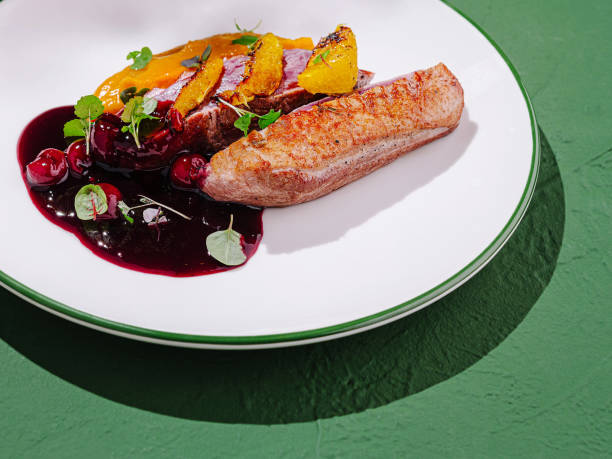 Culinary masterpiece featuring roasted duck breast with berry sauce and citrus garnish served on white plate