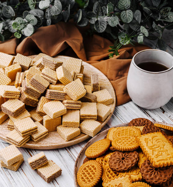 istock Assorted cookies and wafers displayed on wooden table with coffee cup and green foliage 2201009017