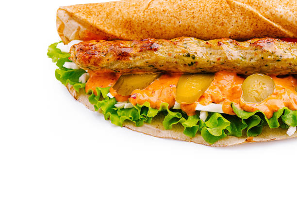A flavorful wrap features a grilled chicken skewer atop crisp lettuce and tangy pickles, all drizzled with a spicy sauce and nestled in a warm flatbread.