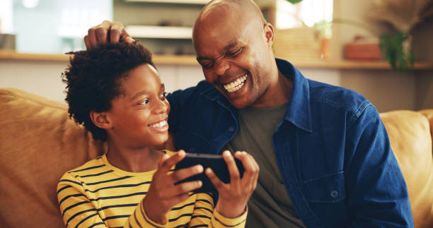 istock Playing, dad and child with smartphone, home and bonding with video game, laughing and fun for score. House, man and gamer with mobile app in lounge, African and boy with hobby, subscription or break 2201017435