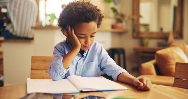 istock African boy, books and bored with homework, frustrated or learning disability with thinking in family home. Kid, notebook and annoyed with reading, study or tired with dyslexia for education in house 2201017466