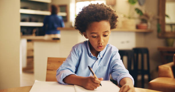 istock Writing, serious and child with homework, home and boy with info, education and studying for exam. Desk, growth and development of kid, knowledge and preparing for test, African and notebook in house 2201017472