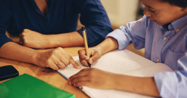istock Mother, child and hands at books for writing, education and help with math homework in home. Woman, kid and learning at table with explaining, advice and homeschooling for knowledge development 2201017527