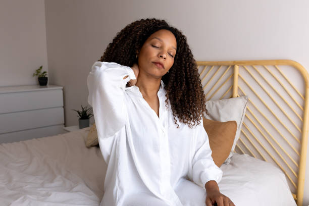 istock Young woman waking up and stretching neck in bed 2201017905