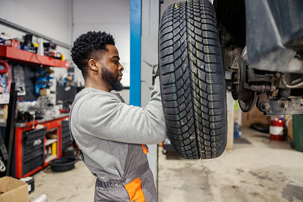 istock Side view of hardworking black auto mechanic changing tire and fixing car at mechanic workshop. 2201019019