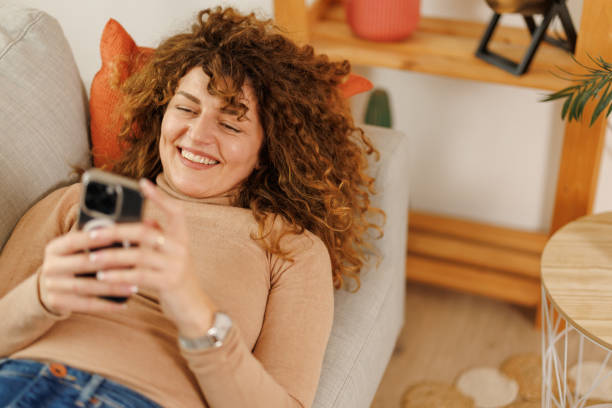 istock Happy woman using phone while relaxing at home 2201019386